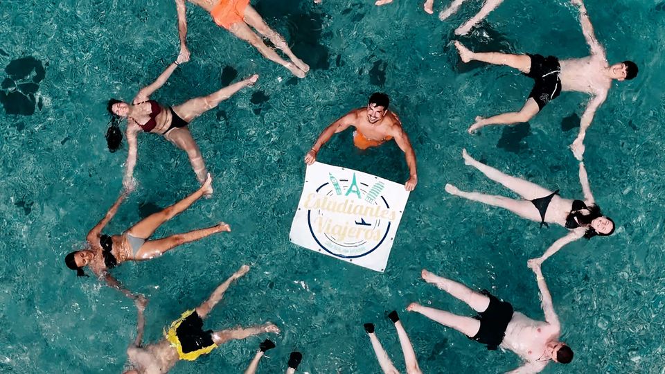 Viajeros de Estudiantes Viajeros formando un círculo en el agua con la bandera de la marca